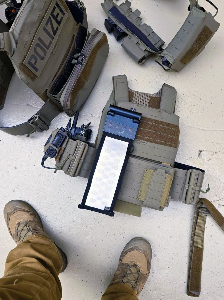 XP ALPHA on an olive-green tactical plate carrier with POLIZEI vest and gear laid out on the floor