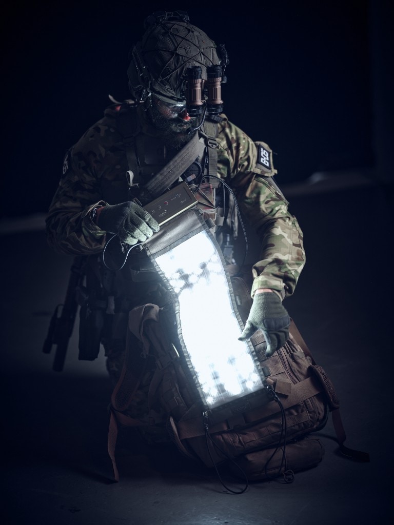 Soldier in tactical gear demonstrating a bright flexible XP DELTA LED panel over a backpack in low light