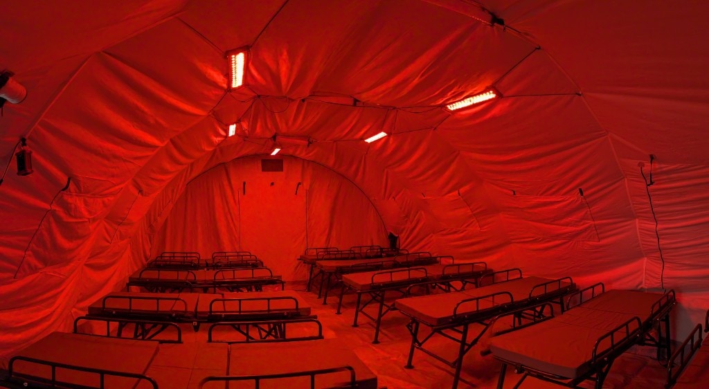 Field medical tent interior lit red by ceiling-mounted XP TENTACLE LED panels, rows of cots