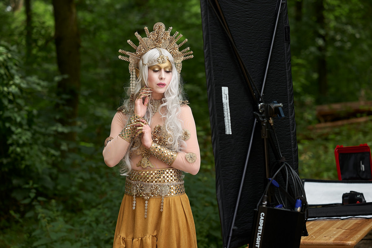 Outdoor-Fotoshooting im Wald: Model im goldenen Kostüm, daneben eine Carpetlight Carpetino am Stativ